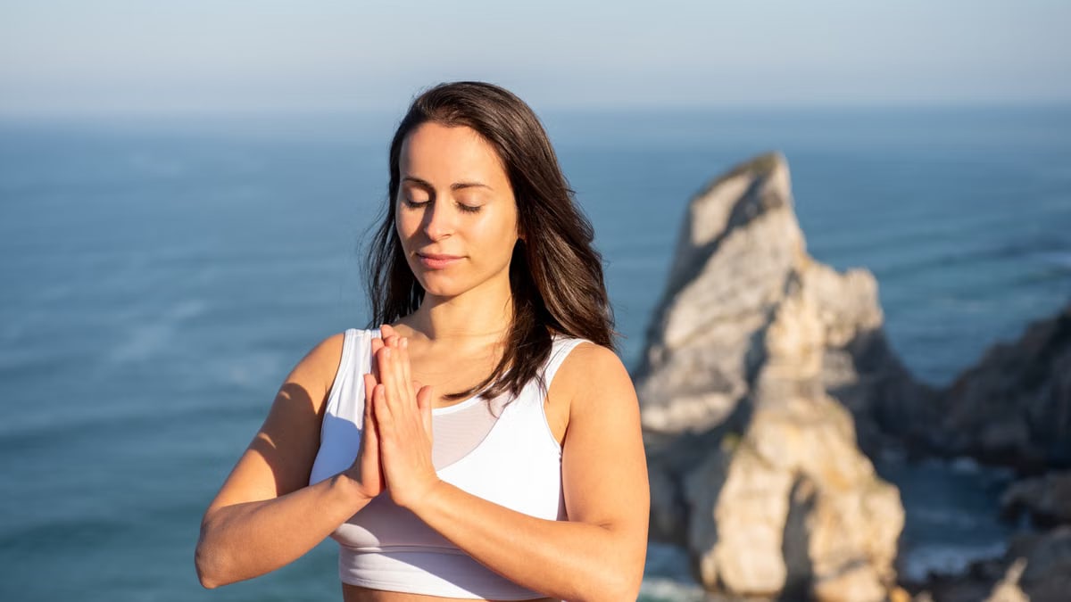 Woman meditating outdoors by the ocean in Portugal, promoting relaxation and mindfulness.